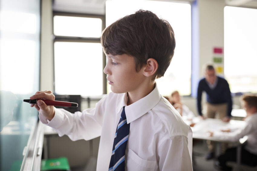 Schoolboy writing on whiteboard in classroom