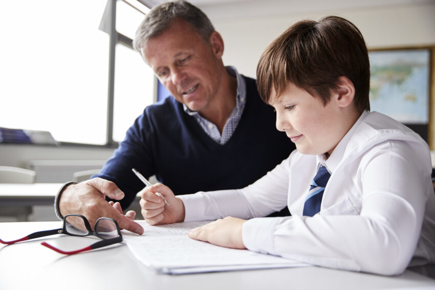 High School Tutor Giving Male Student Wearing Uniform One To One Tuition At Desk