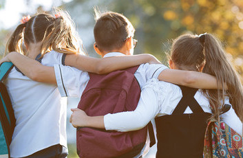 Three schoolchildren with backpacks embracing outdoors